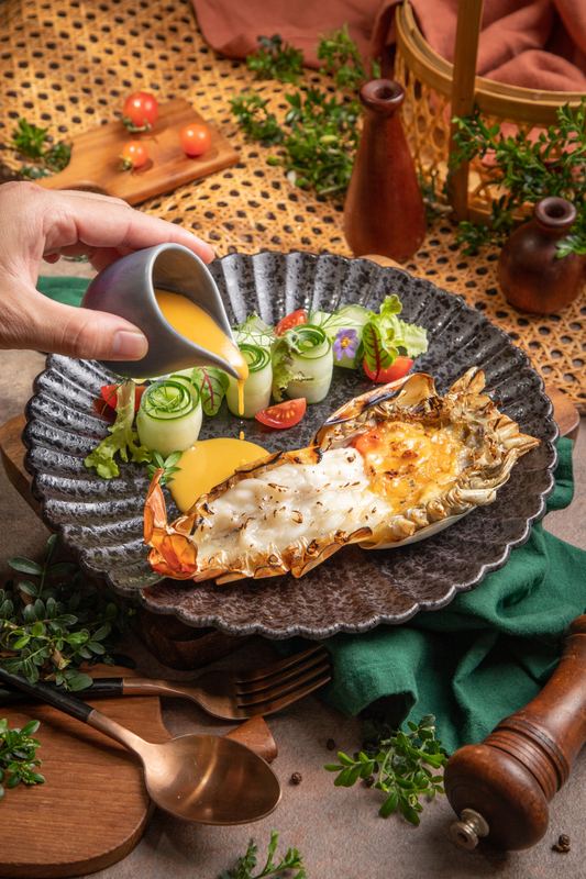 Curry wird am Tisch über einen gegrillten Langustenschwanz gegossen