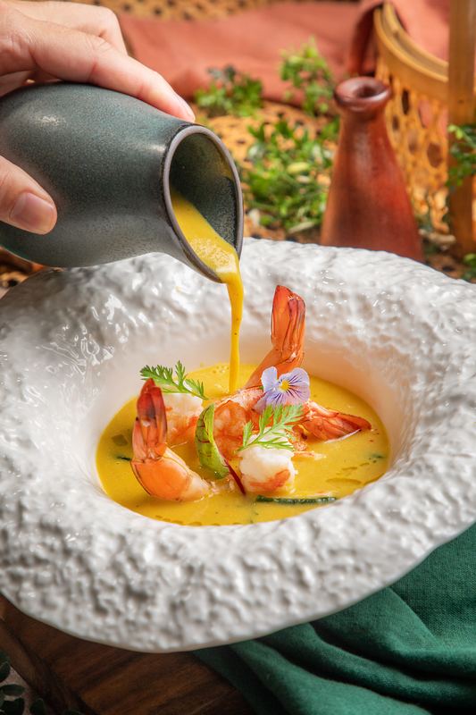 Gelbe Currysuppe mit Garnelen wird am Tisch aufgegossen