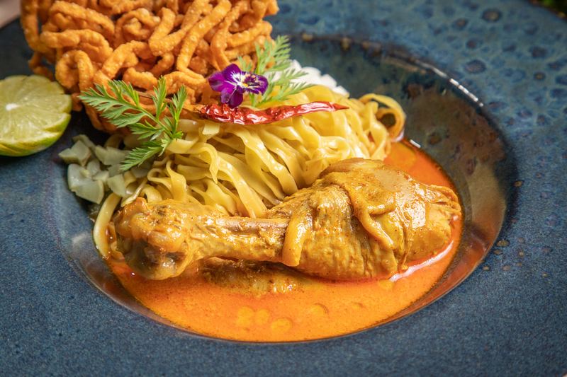 Khao Soi mit Hühnerschenkel, Eiernudeln und knusprigen Nudeln in Kokos-Curry